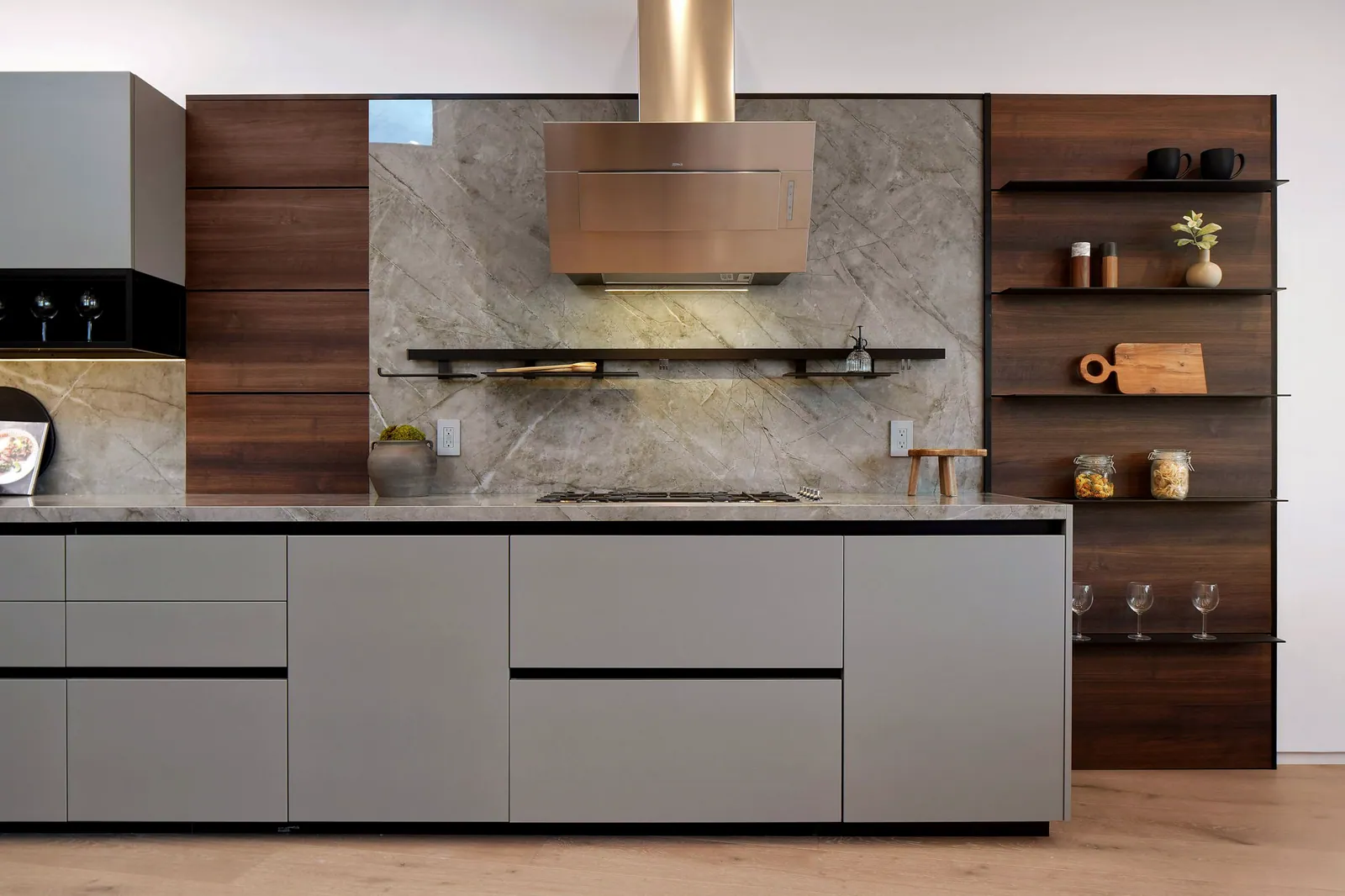 Kitchen wall with green-gray flat-panel cabinets, a stone backsplash, a brass range hood, and walnut open shelves
