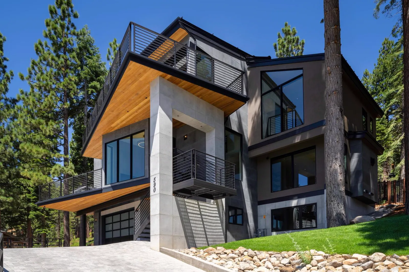 Exterior of the three-story home with wood soffits, concrete, and dark windows among pine trees