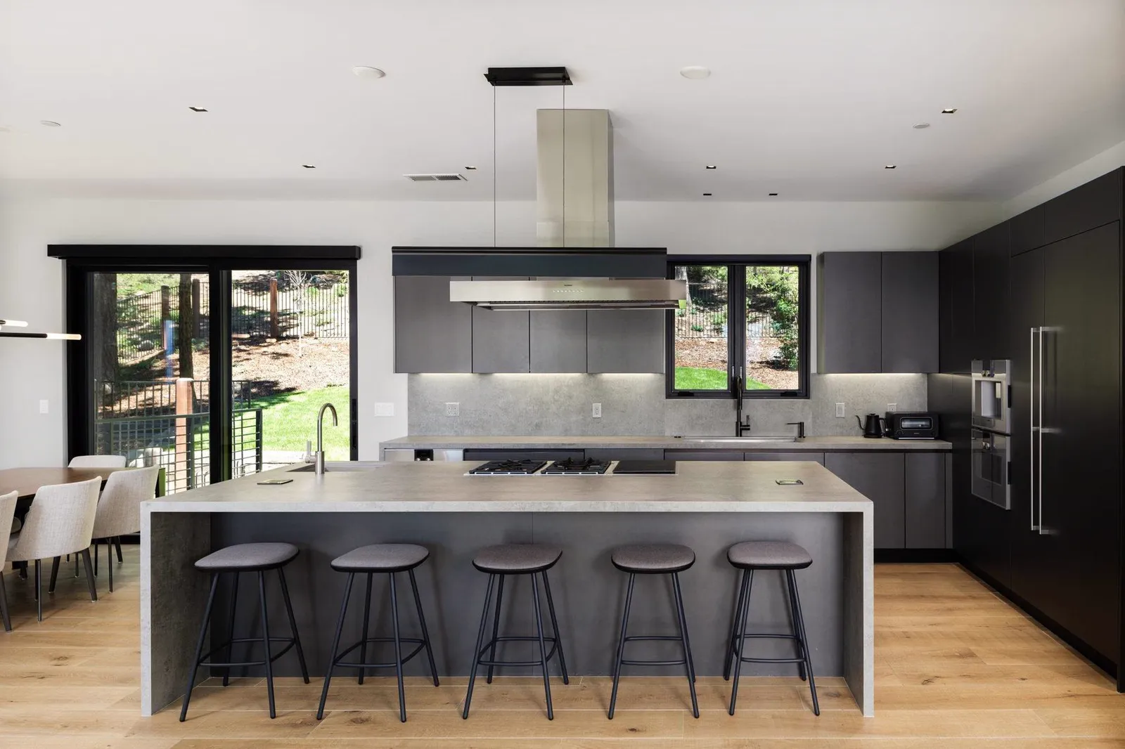 Kitchen with a gray island, bar stools, stainless hood, and dark tall cabinets