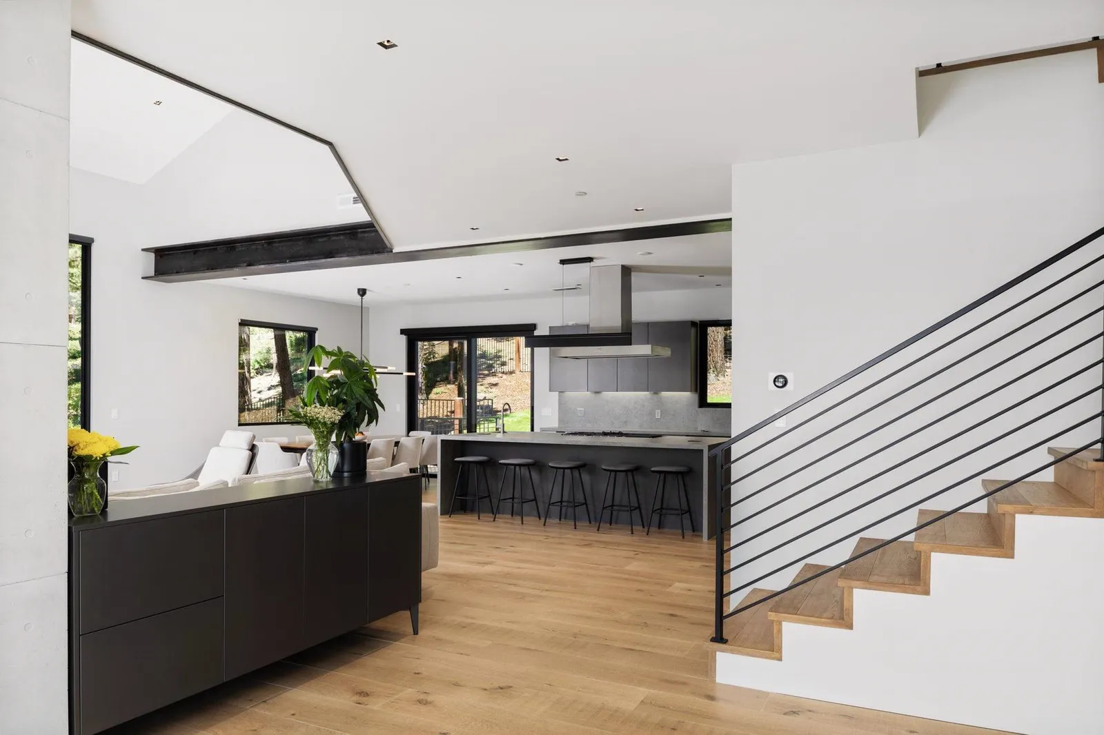 Living area with a dark kitchen island beyond and a stair with a black railing