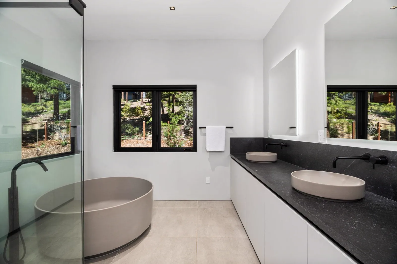 Bathroom with a round stone-gray tub, black vanity counter, and vessel sinks