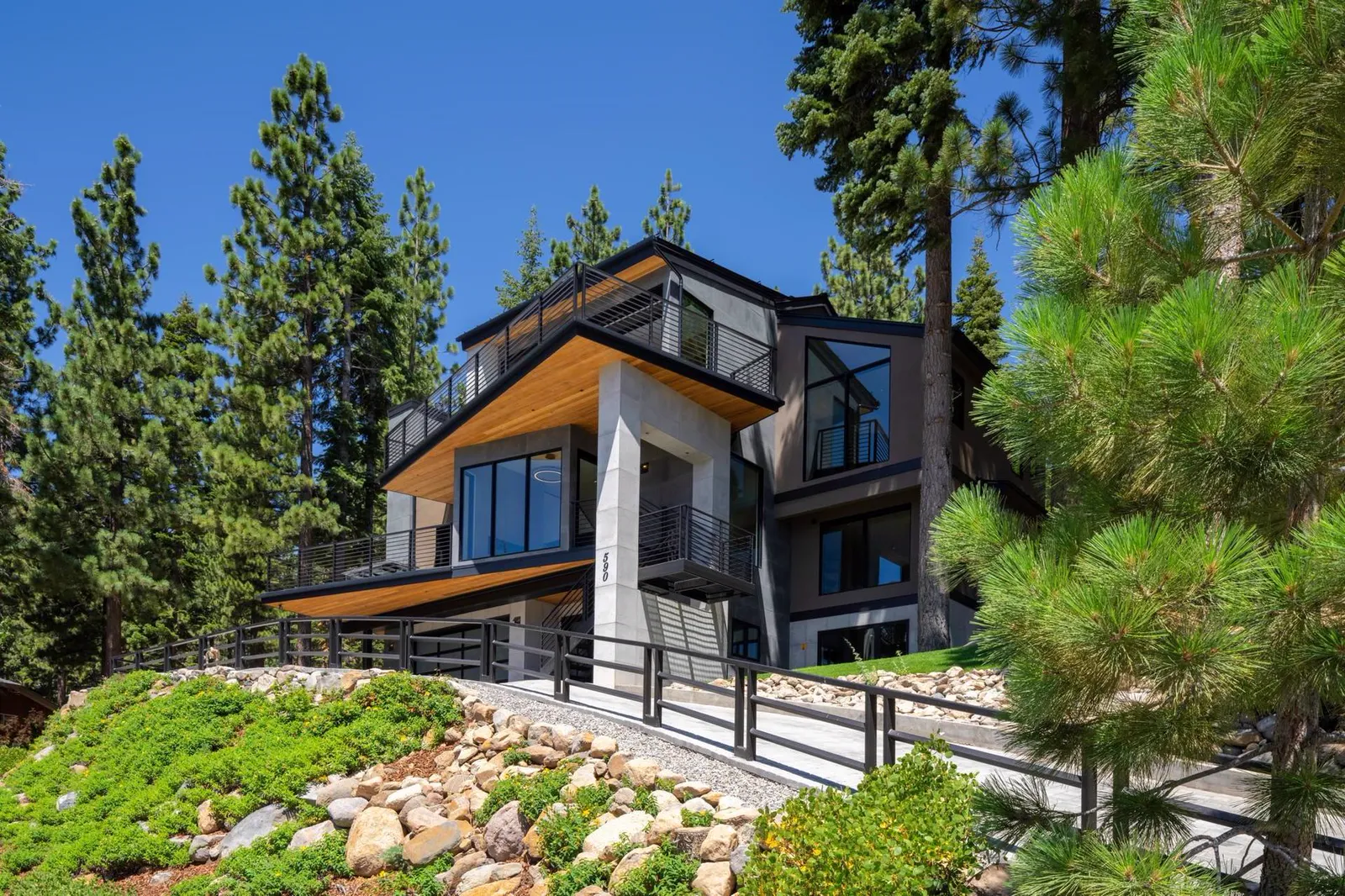Exterior of the home among pine trees with landscaped slopes