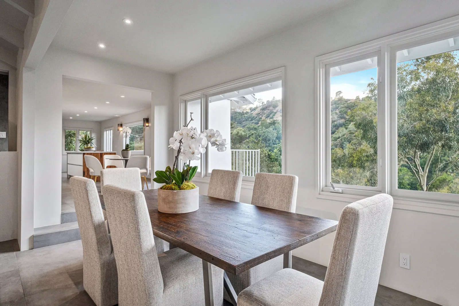 Dining room with a wood table and white upholstered chairs beside windows facing the canyon