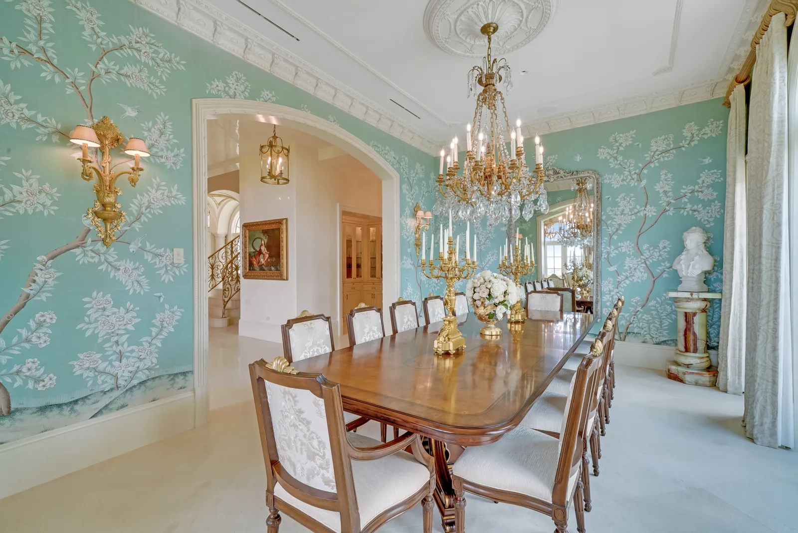Dining room with hand-painted blue-green wallpaper, a crystal chandelier, and a long table