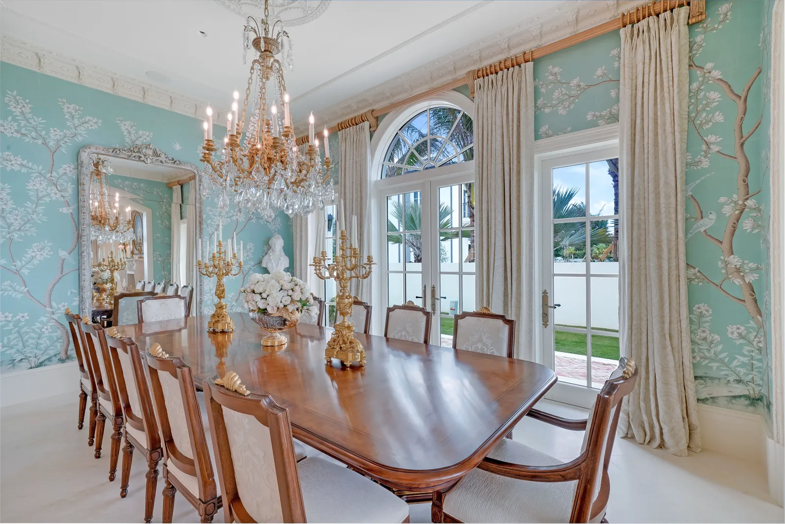 Dining room with a long wood table, crystal chandelier, and arched French doors