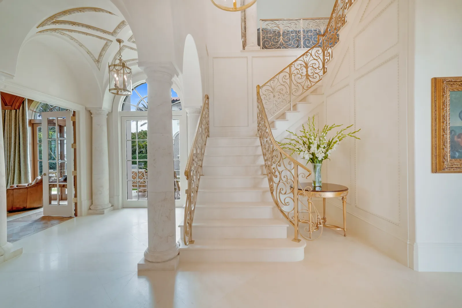 Stair hall with a curved staircase, gilded iron railing, and stone columns