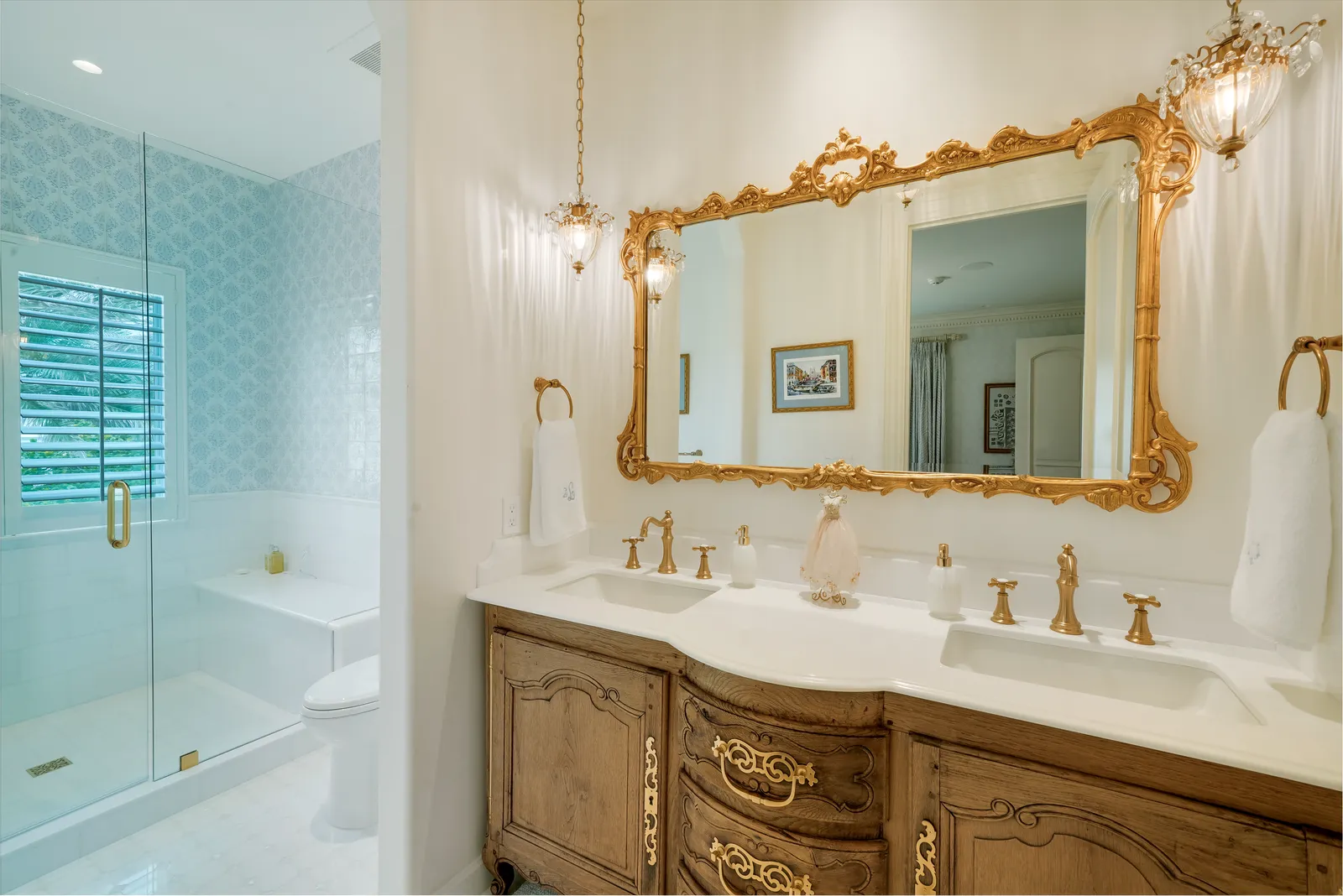 Bathroom with a carved wood vanity, gilded mirror, and glass shower