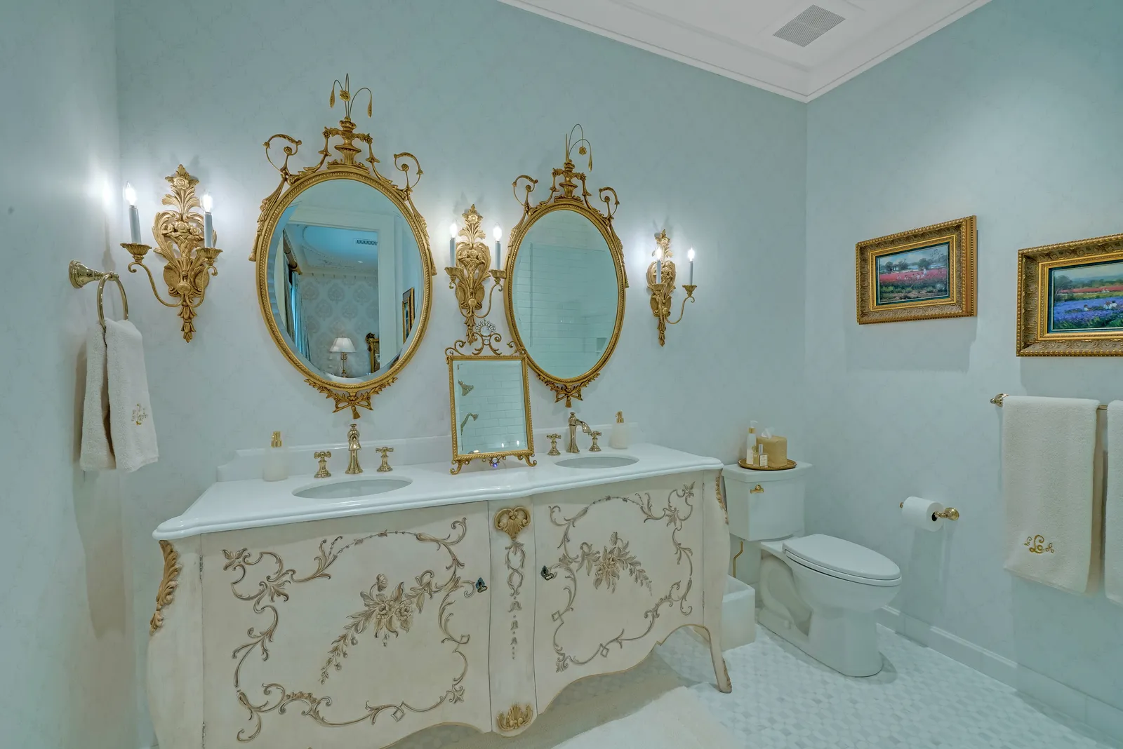 Powder room with a carved white and gold vanity and oval gilded mirrors