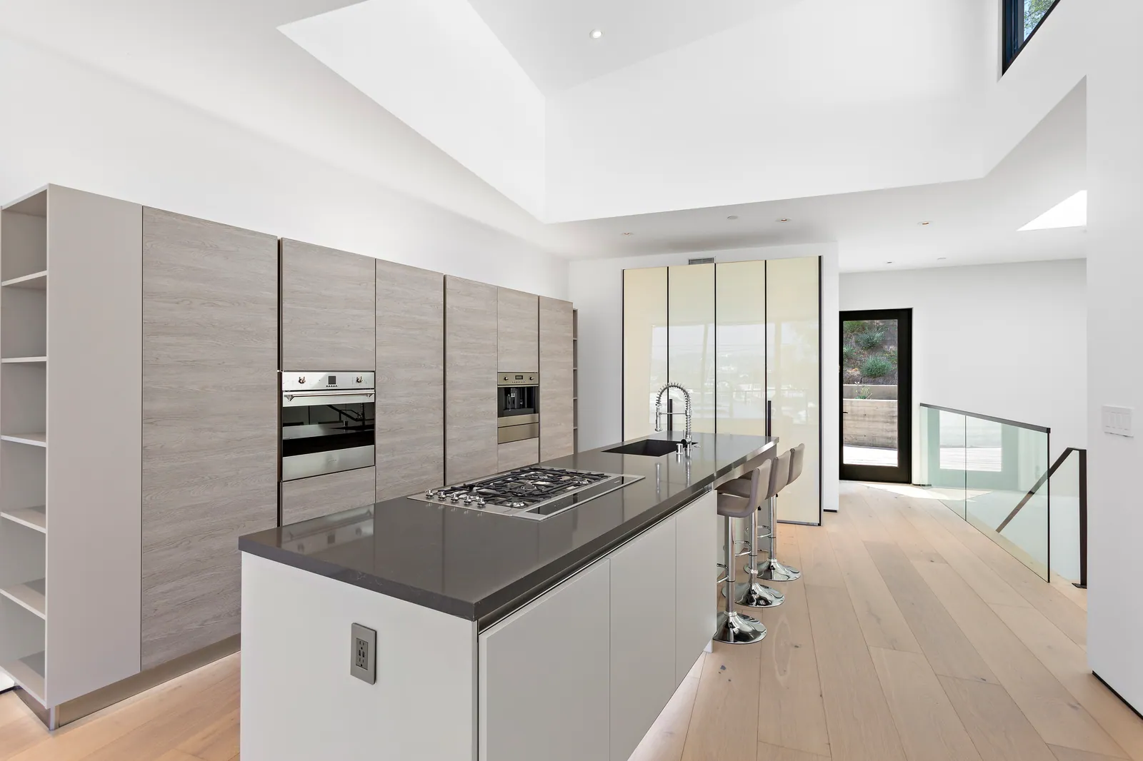 Kitchen with tall gray oak cabinetry, built-in ovens, and a white island with a dark countertop