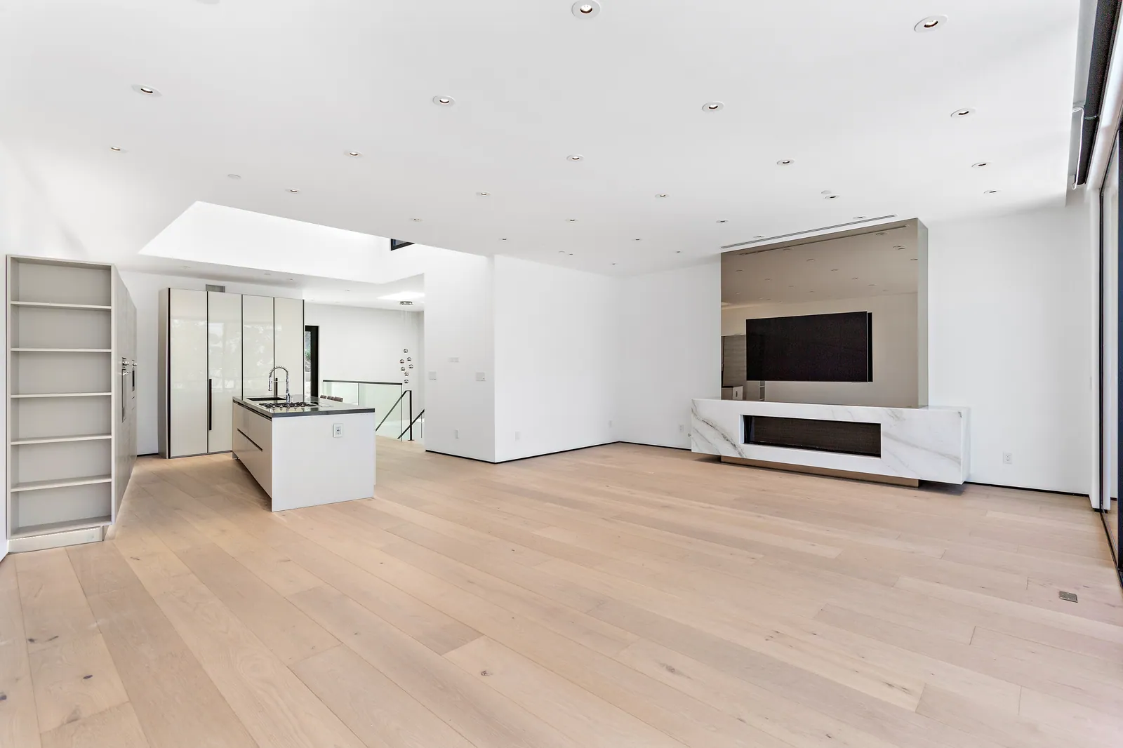 Open living area with light oak floors, the kitchen island, and a white media wall