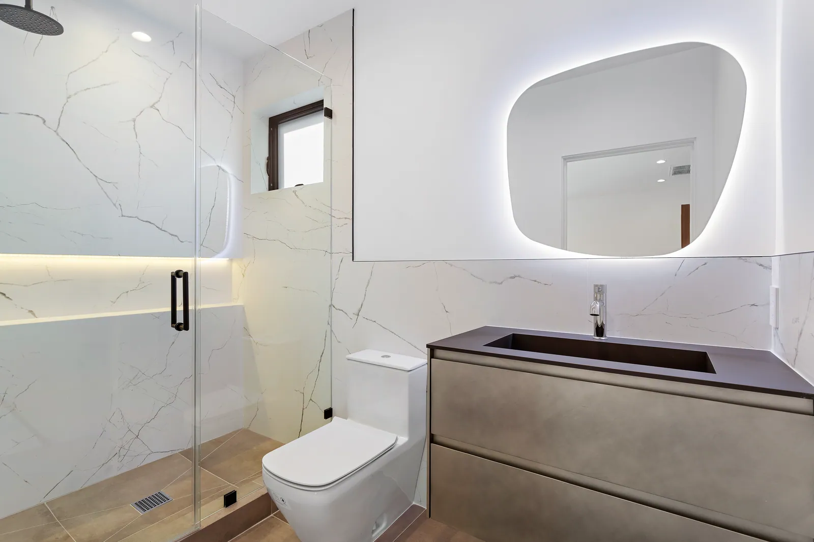 Bathroom with marble-look walls, a backlit mirror, and a gray floating vanity