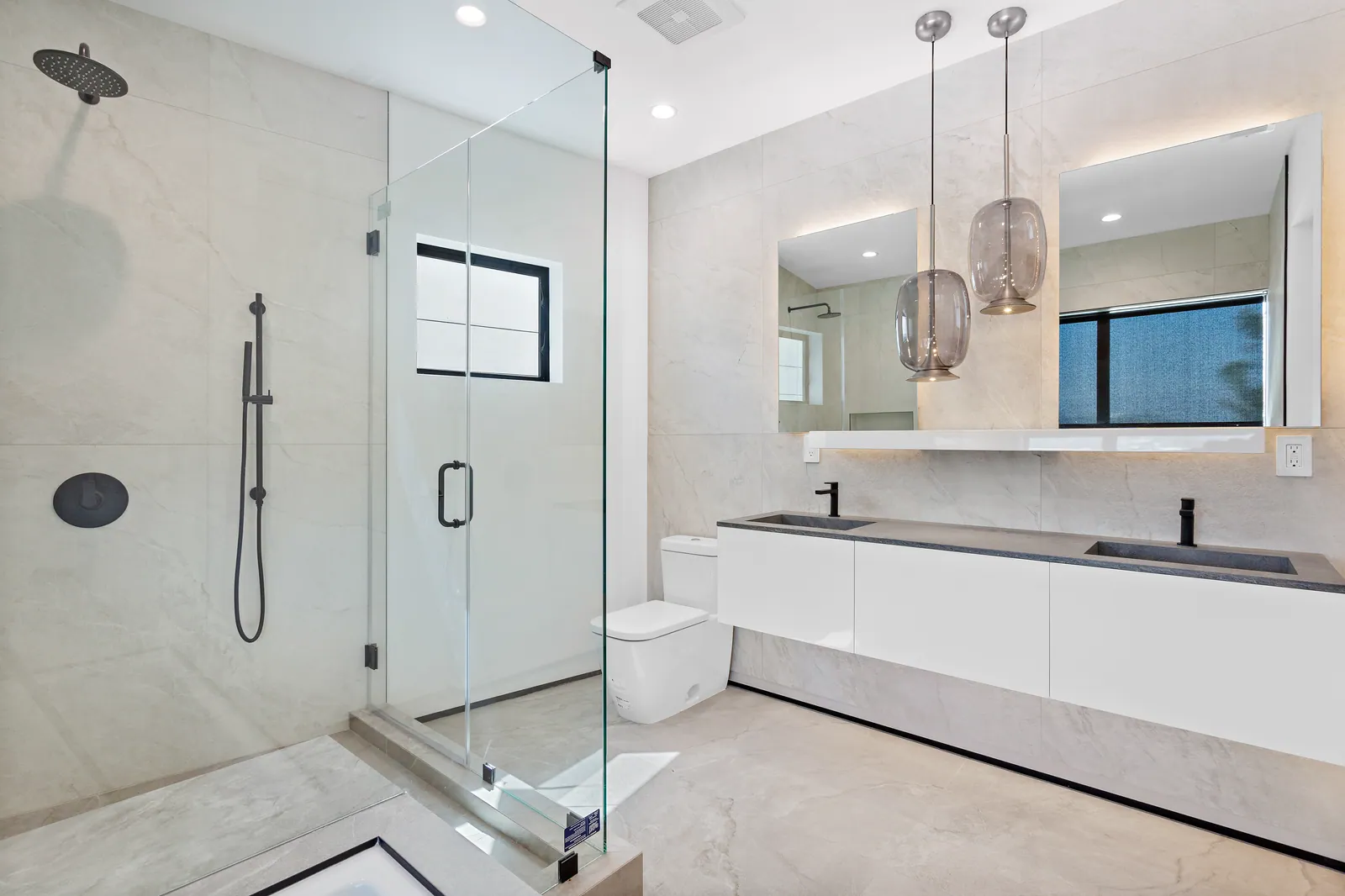 Bathroom with a double vanity, glass shower, and pendant lights