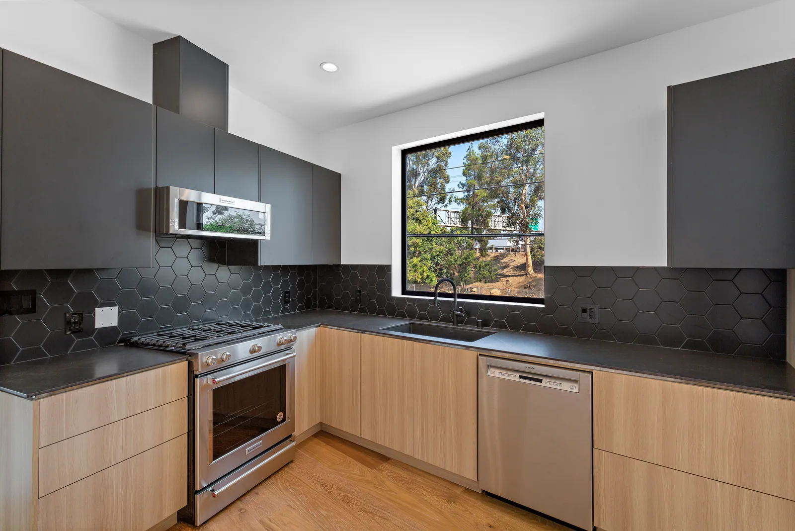Kitchen with light wood lower cabinets, dark upper cabinets, and a dark tile backsplash