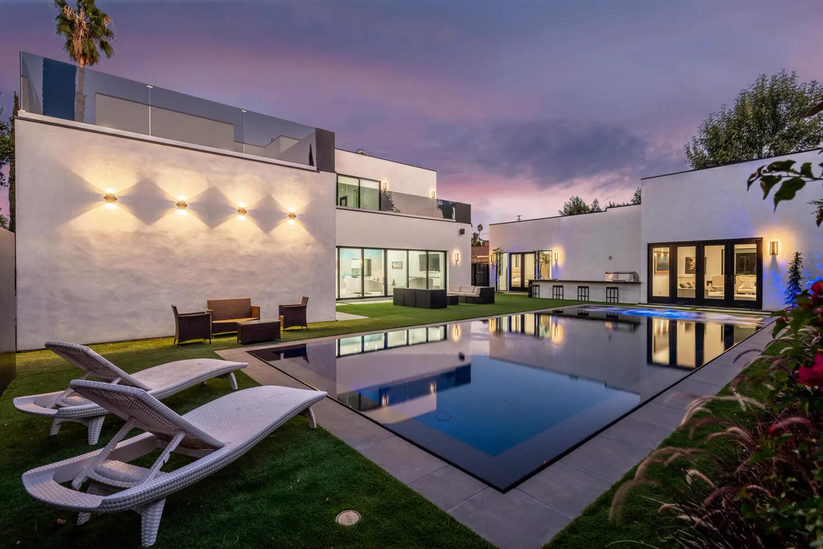Pool and lounge chairs behind the white modern house at dusk