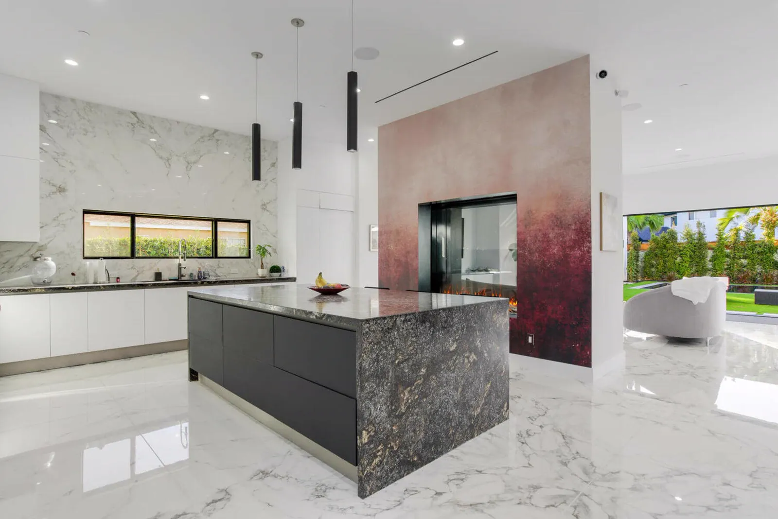 Kitchen with a dark granite island, white marble floors, and a red-toned feature wall with a fireplace
