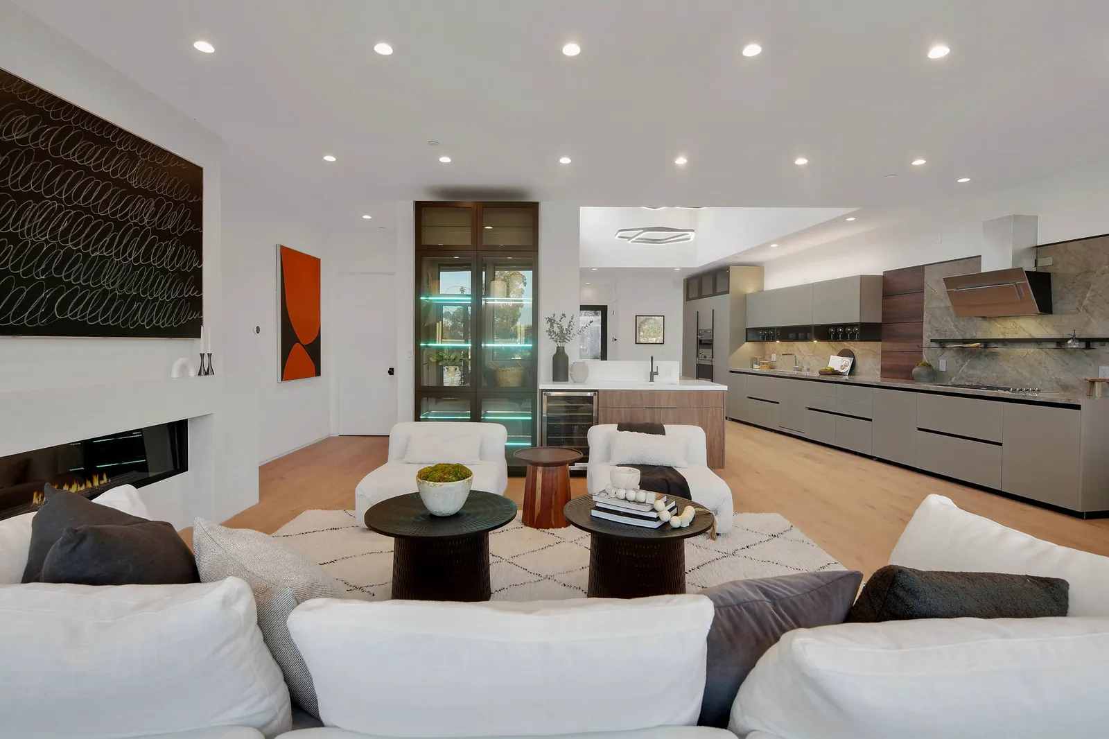 Open living area with white sofas and round black tables, with the kitchen beyond