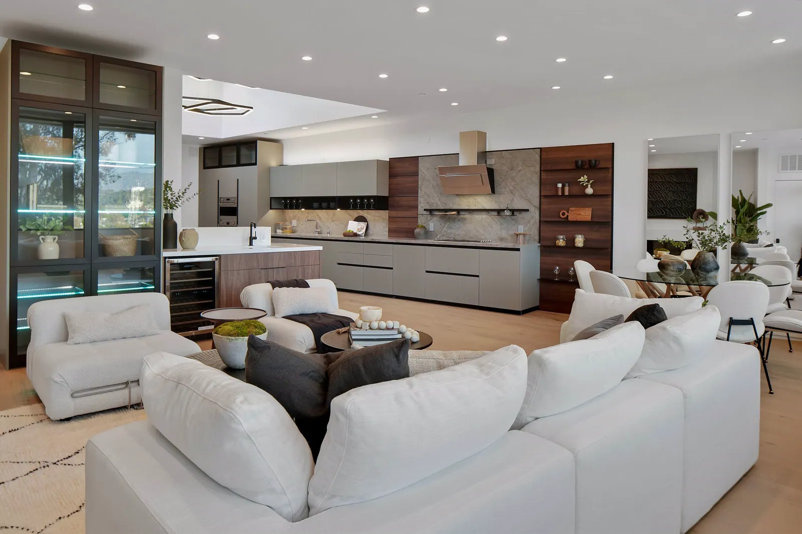 View across the living room to the long kitchen with green-gray cabinetry and walnut shelving