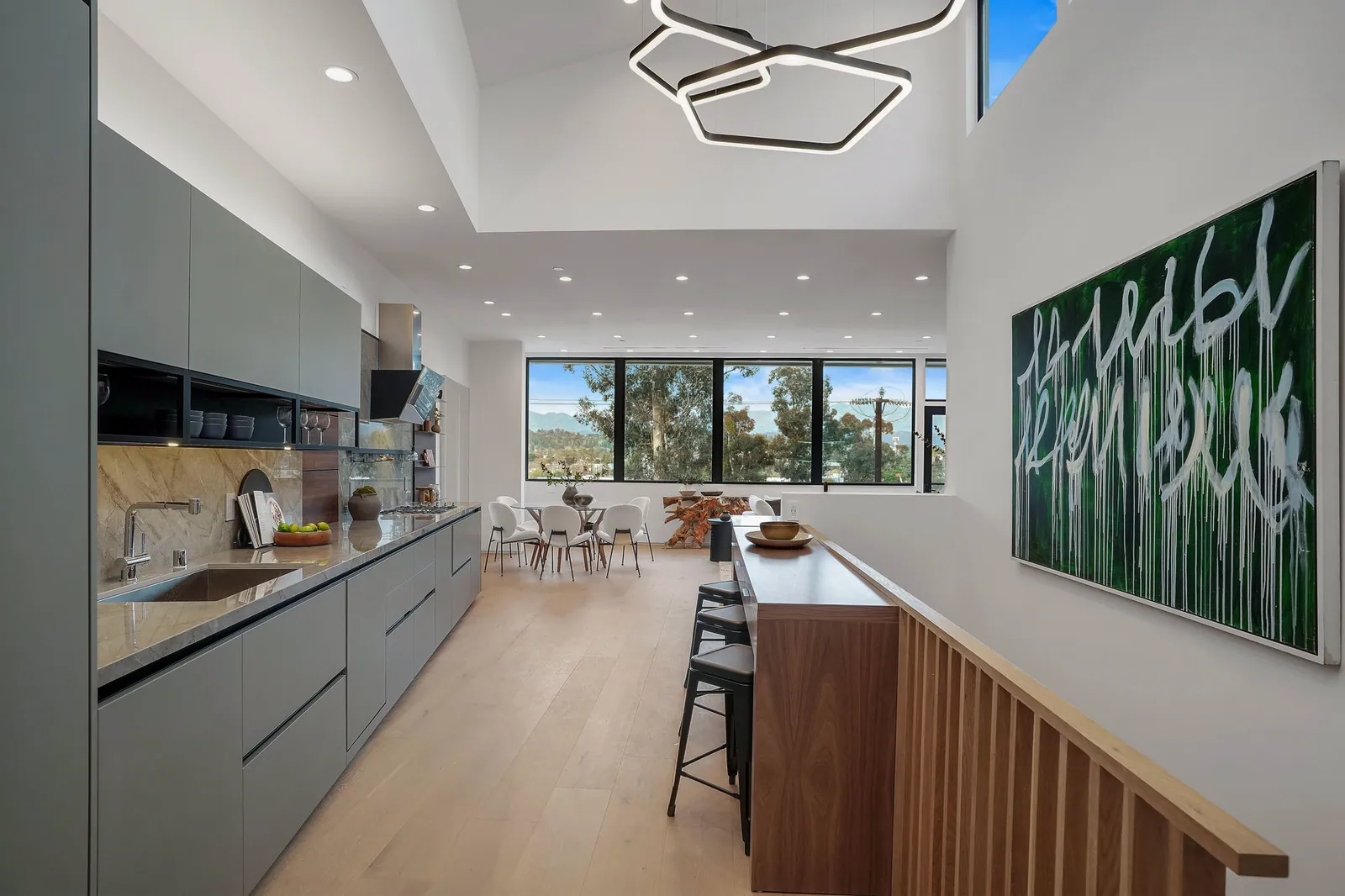Kitchen run and breakfast bar leading to a dining area by the windows, under a geometric pendant light