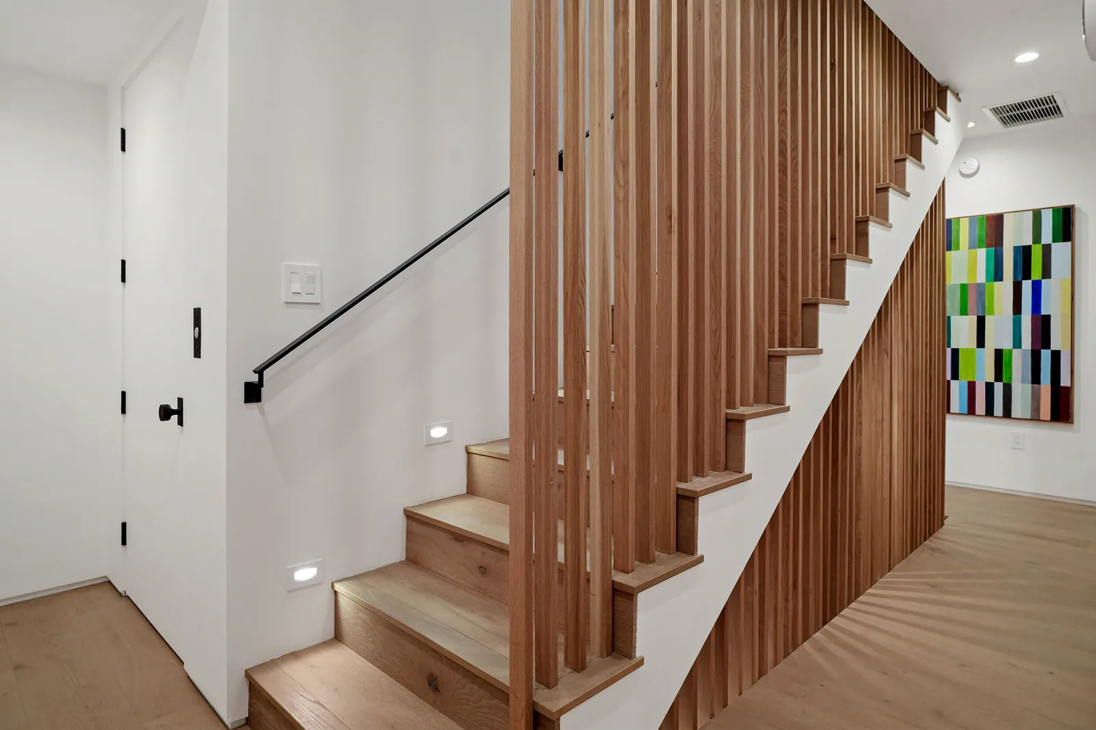 Oak stair with a vertical slat screen and colorful artwork on the wall