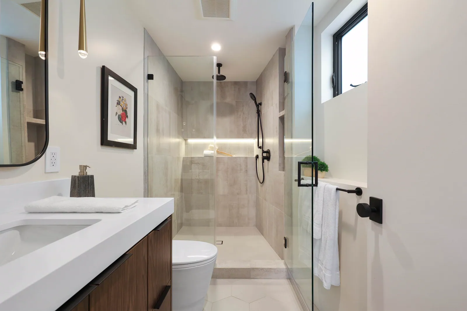 Bathroom with a walnut vanity, white counter, and glass shower with a lit niche