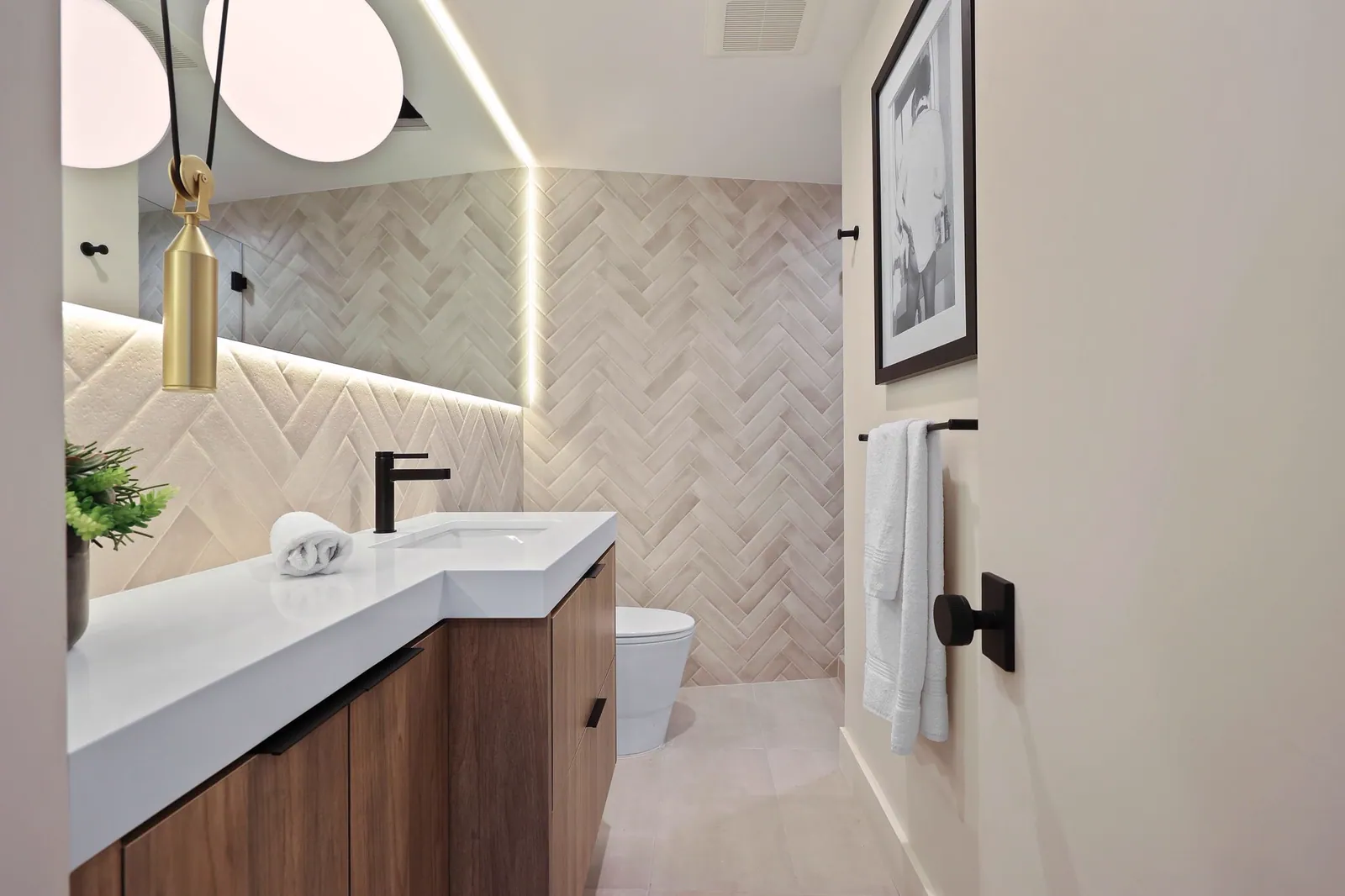 Bathroom vanity with a walnut cabinet, herringbone tile wall, and backlit mirror