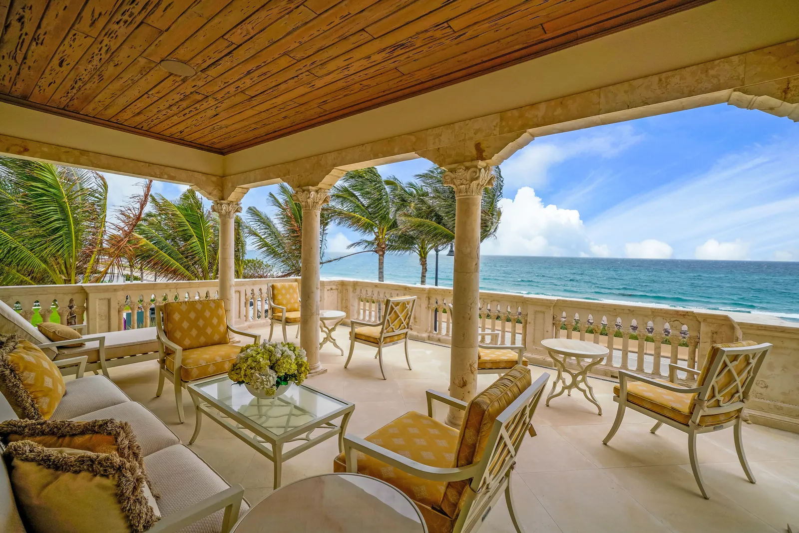 Covered oceanfront loggia with stone columns, a wood ceiling, and outdoor seating facing the Atlantic