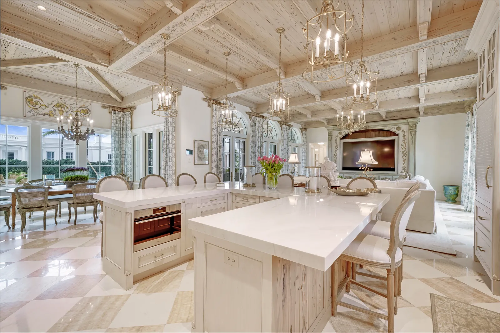 Kitchen with two white islands under a coffered wood ceiling and crystal chandeliers