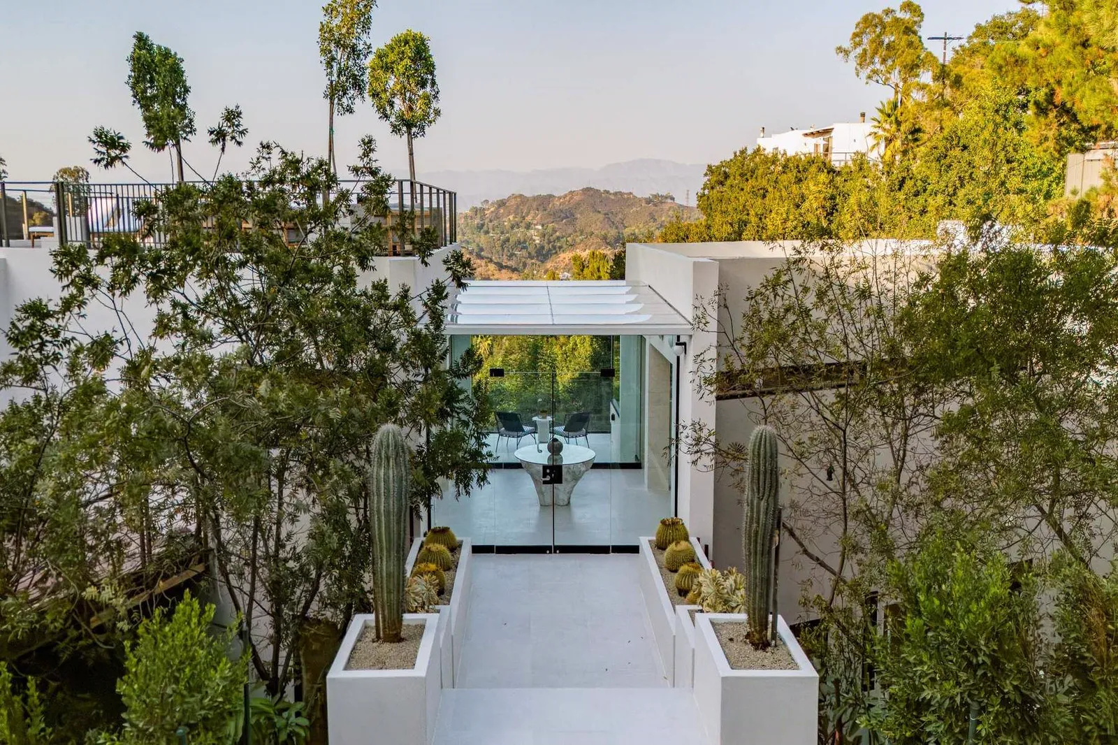 Walkway between planters leading to the glass entry with hillside views