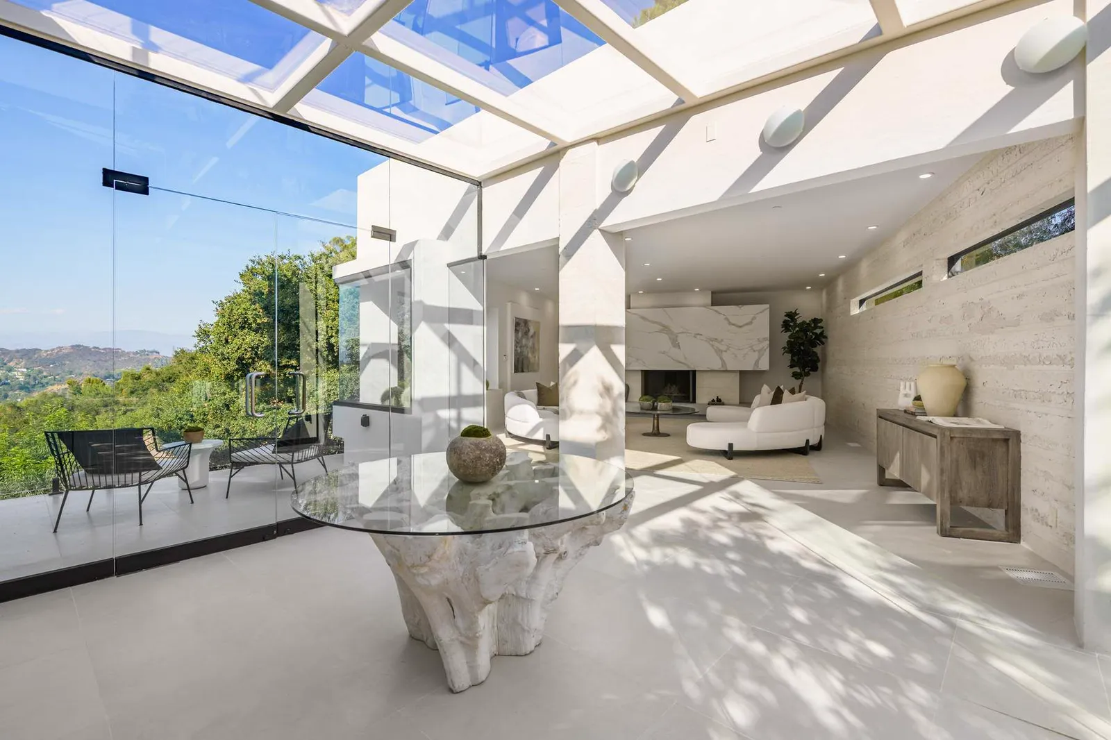 Living area under a glass roof with a round glass dining table and hillside views