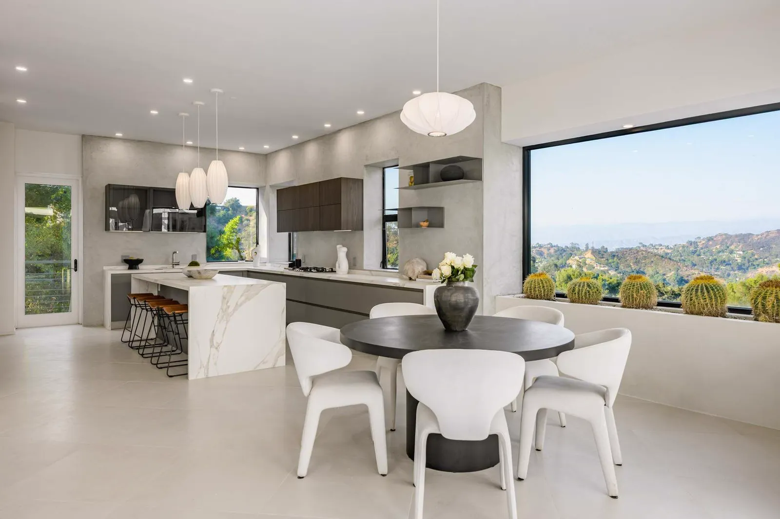 Kitchen and dining area with a marble island, white chairs, and a large picture window