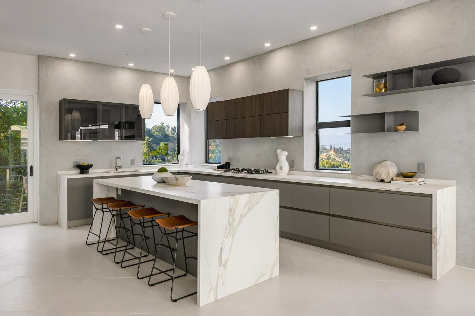 Kitchen with a marble waterfall island, leather counter stools, and dark wood upper cabinets