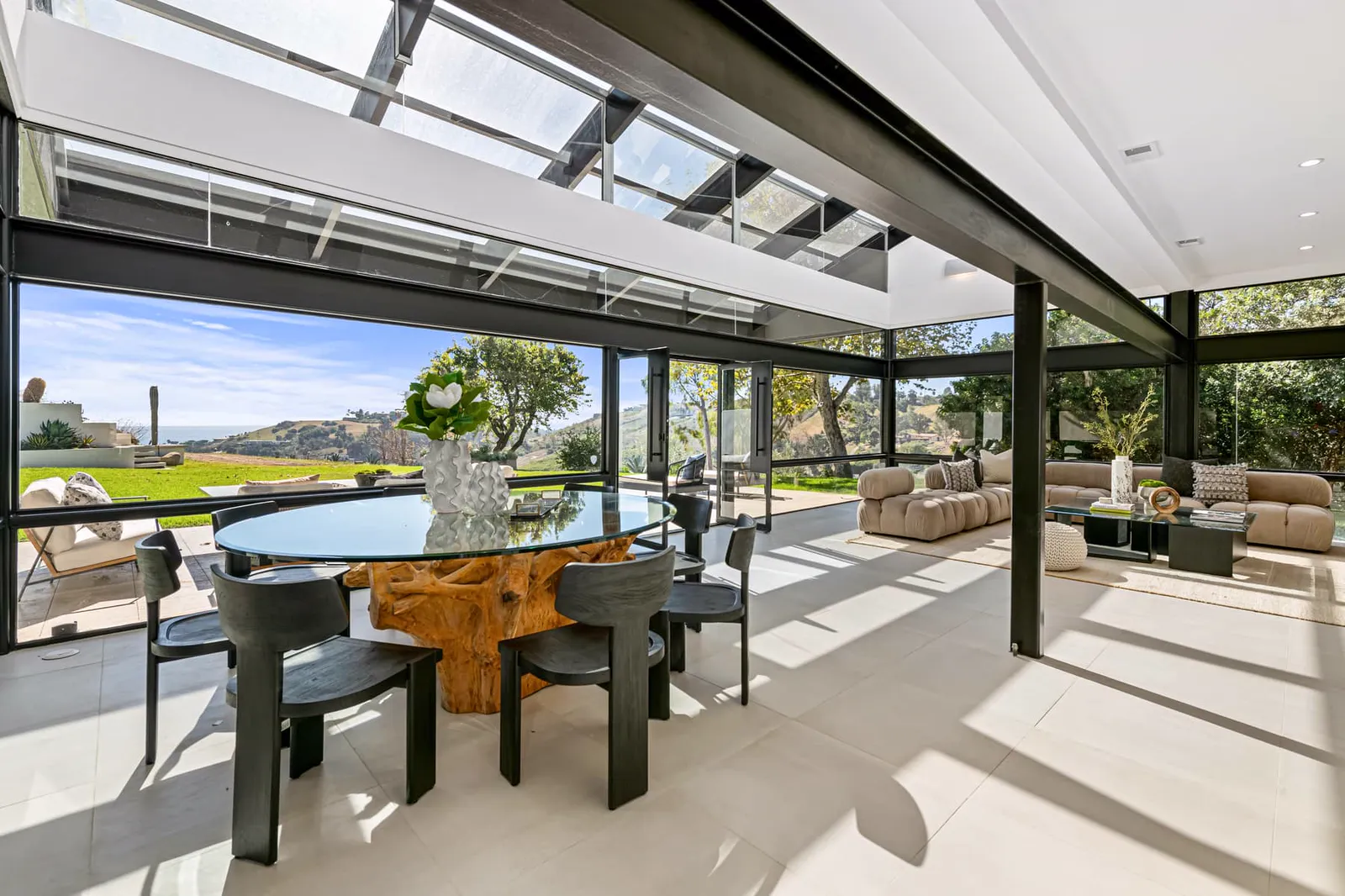 Round dining table beside open glass walls and hillside views