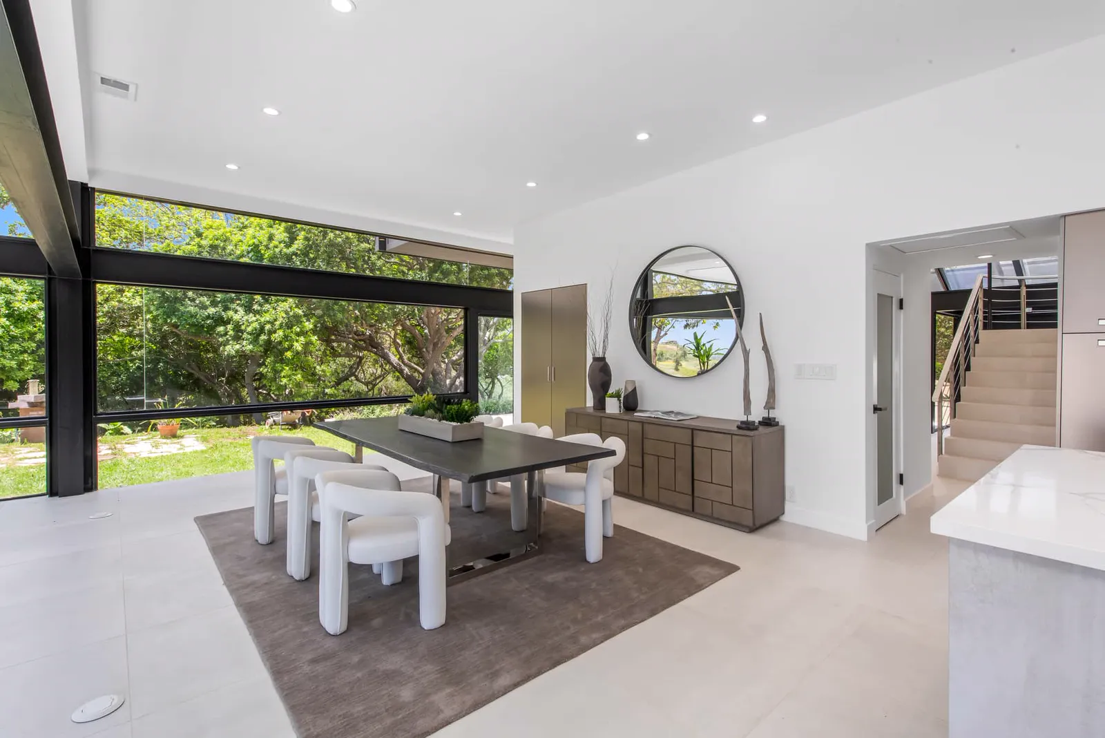 Dining area with sculptural white chairs and a round mirror