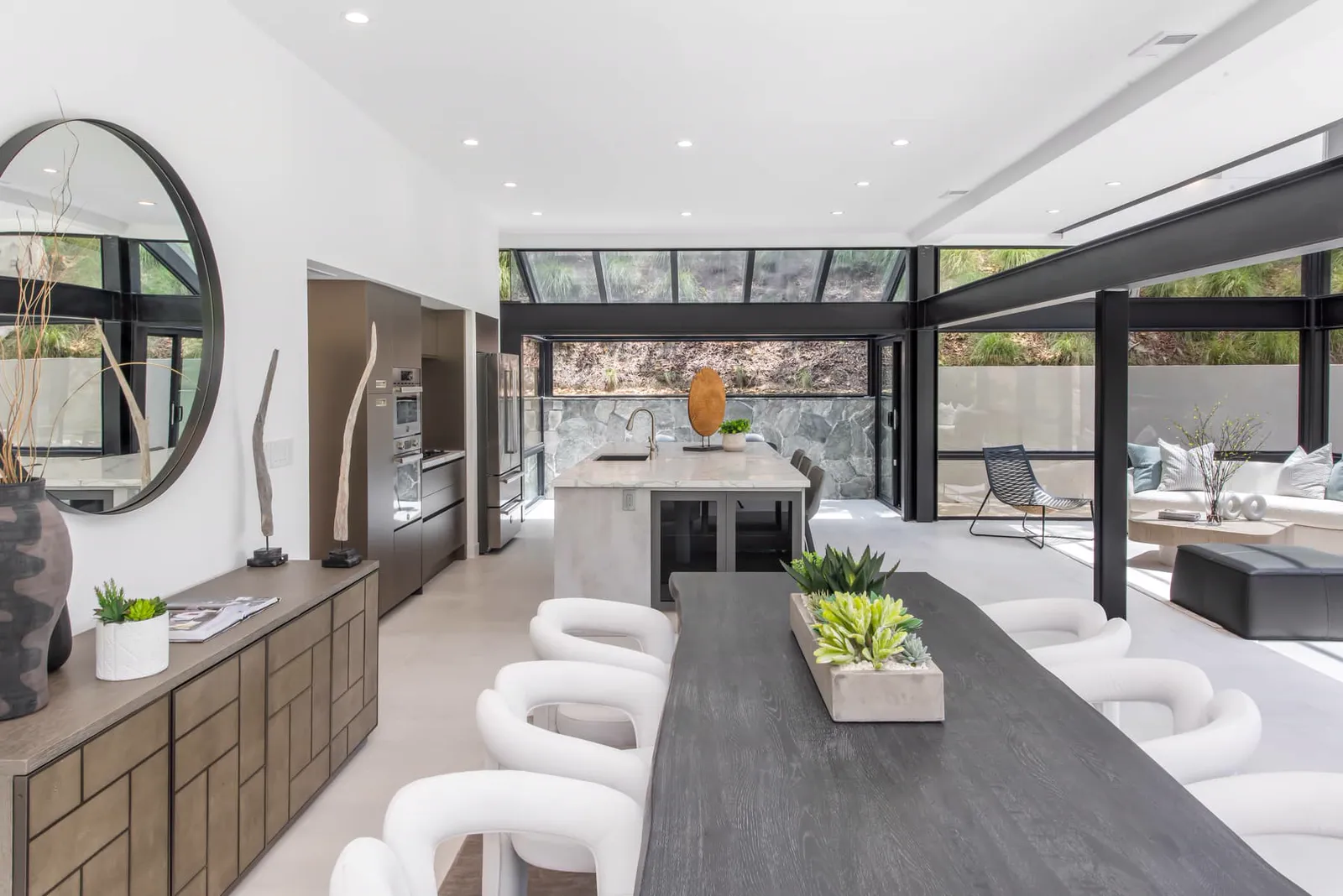 Long dining table with white chairs in front of the kitchen