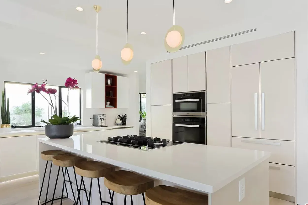 White kitchen with a long island, wood counter stools, and globe pendant lights