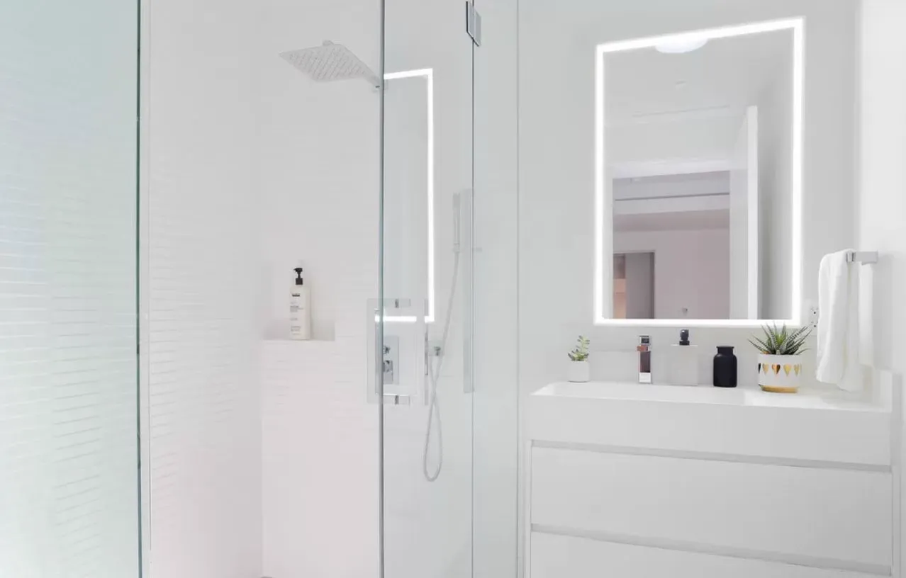 Glass shower and white vanity with a lit mirror