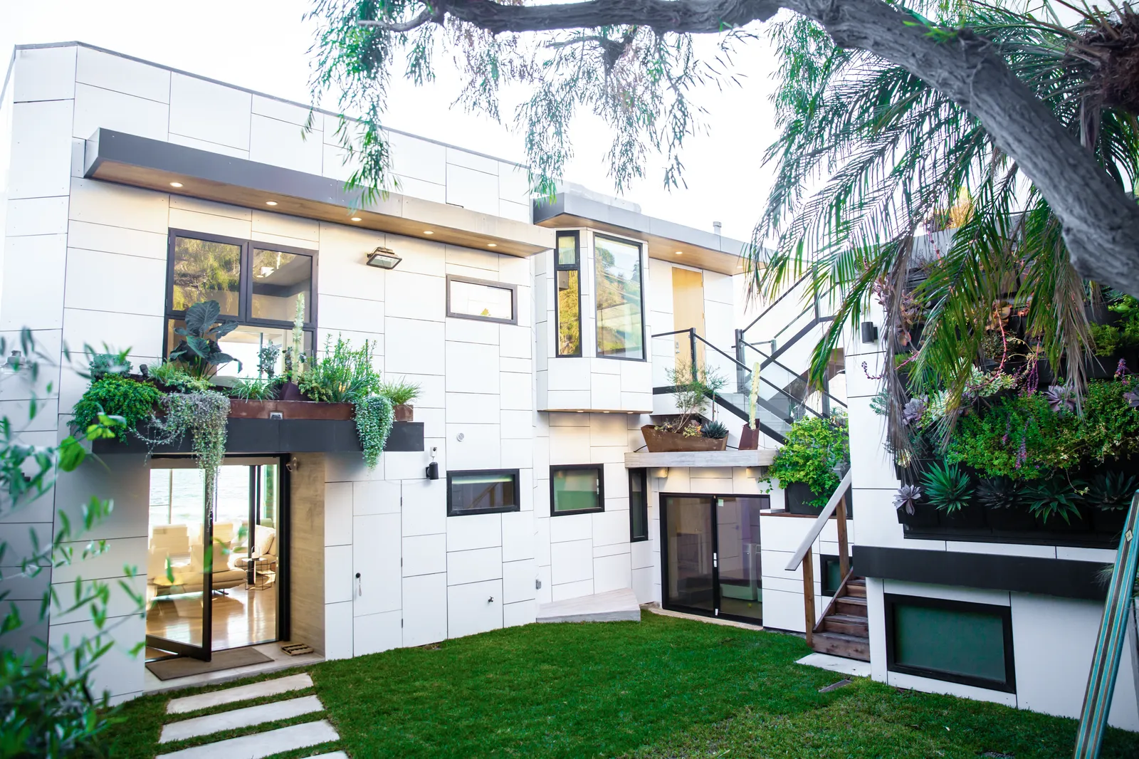 Courtyard with a lawn, stepping stones, and a white panel facade with planters