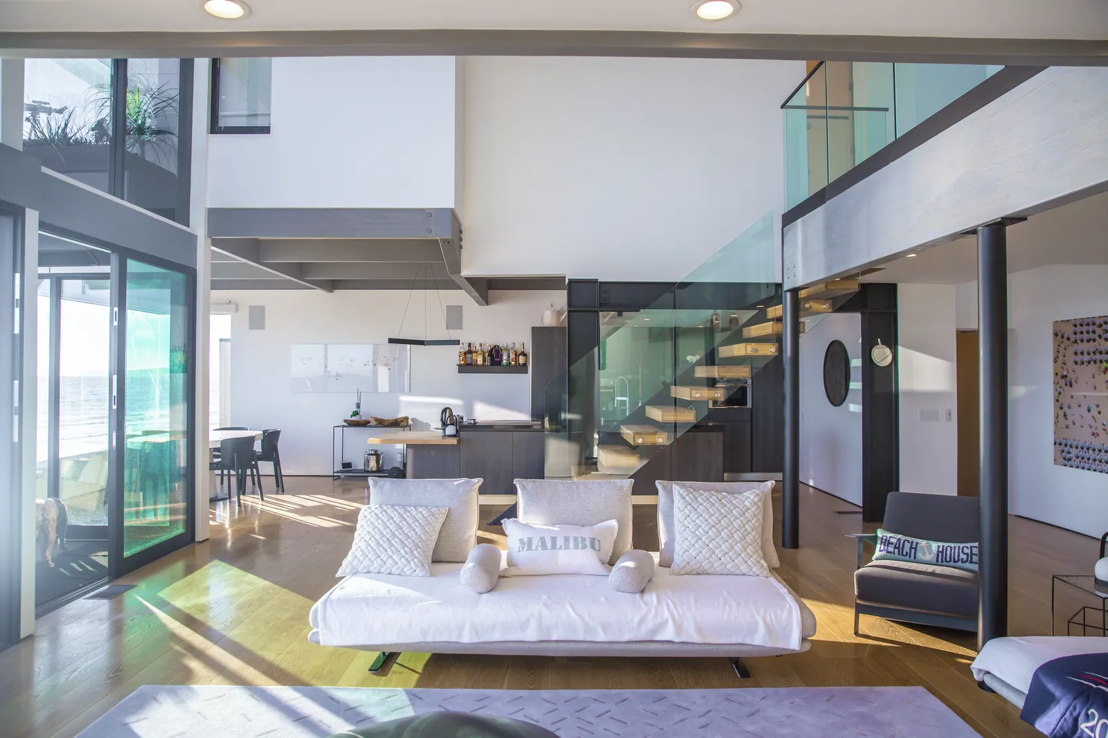 Double-height living room with white sofas, a glass railing, and a floating stair