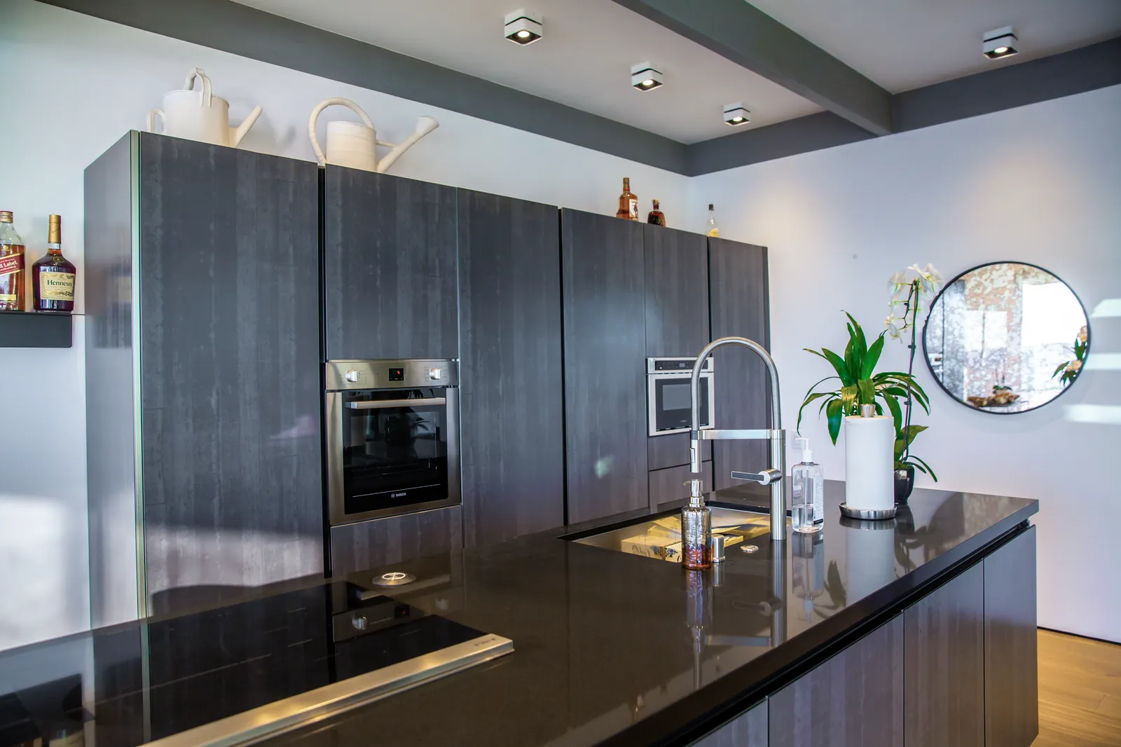 Kitchen with dark tall cabinets, a built-in oven, and a black island counter