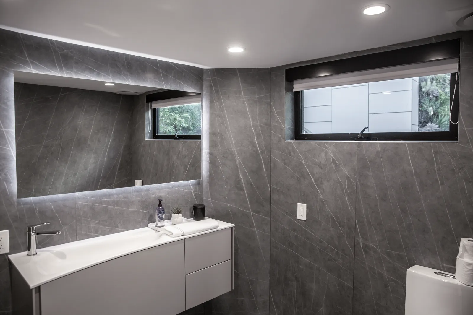 Bathroom with dark stone walls, a floating white vanity, and a backlit mirror