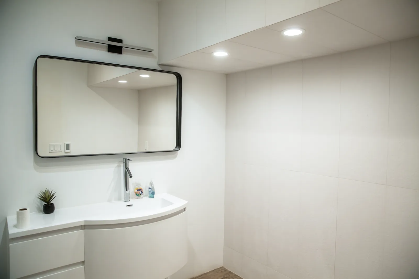 Bathroom with a curved white vanity and a black-framed mirror