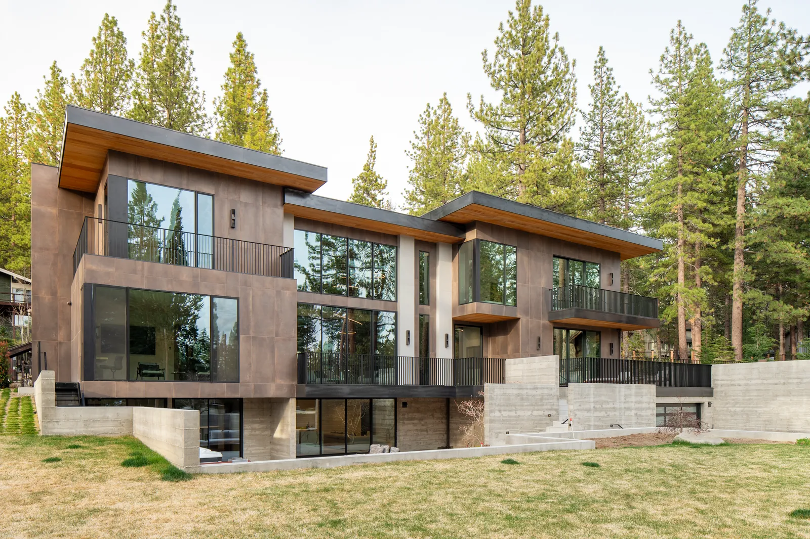 Exterior of the three-story home with wood and stone cladding among tall pines