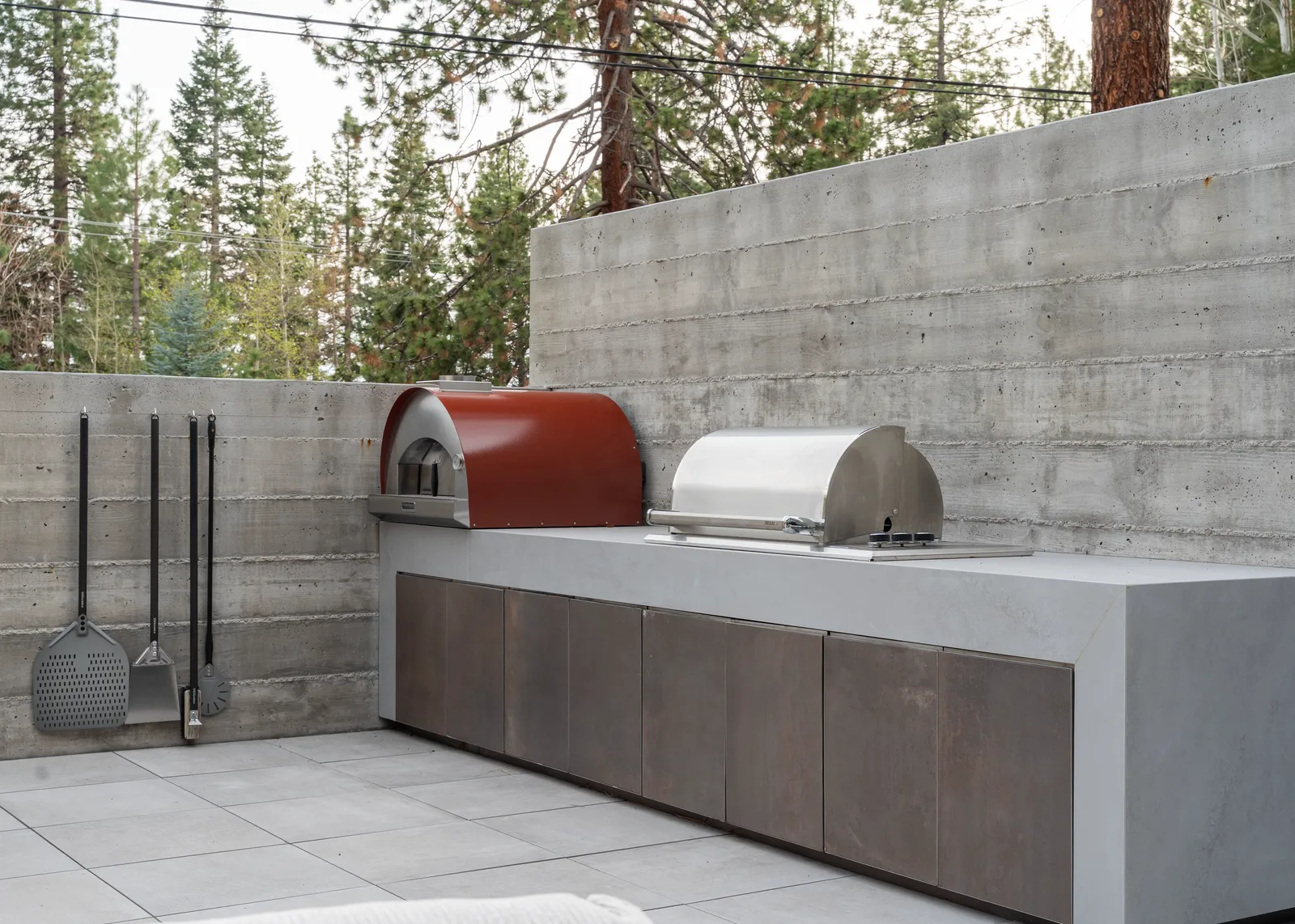 Outdoor kitchen with a pizza oven and grill set against a board-formed concrete wall