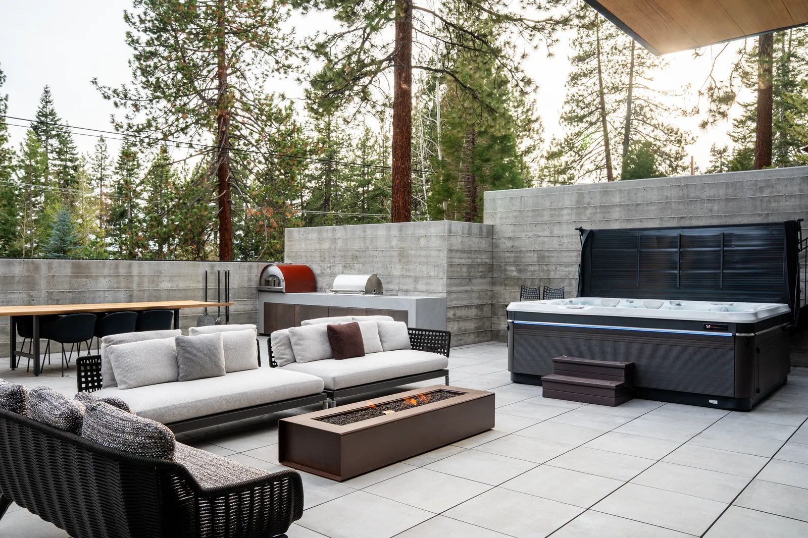 Terrace with sofas, a fire table, and a hot tub against a concrete wall
