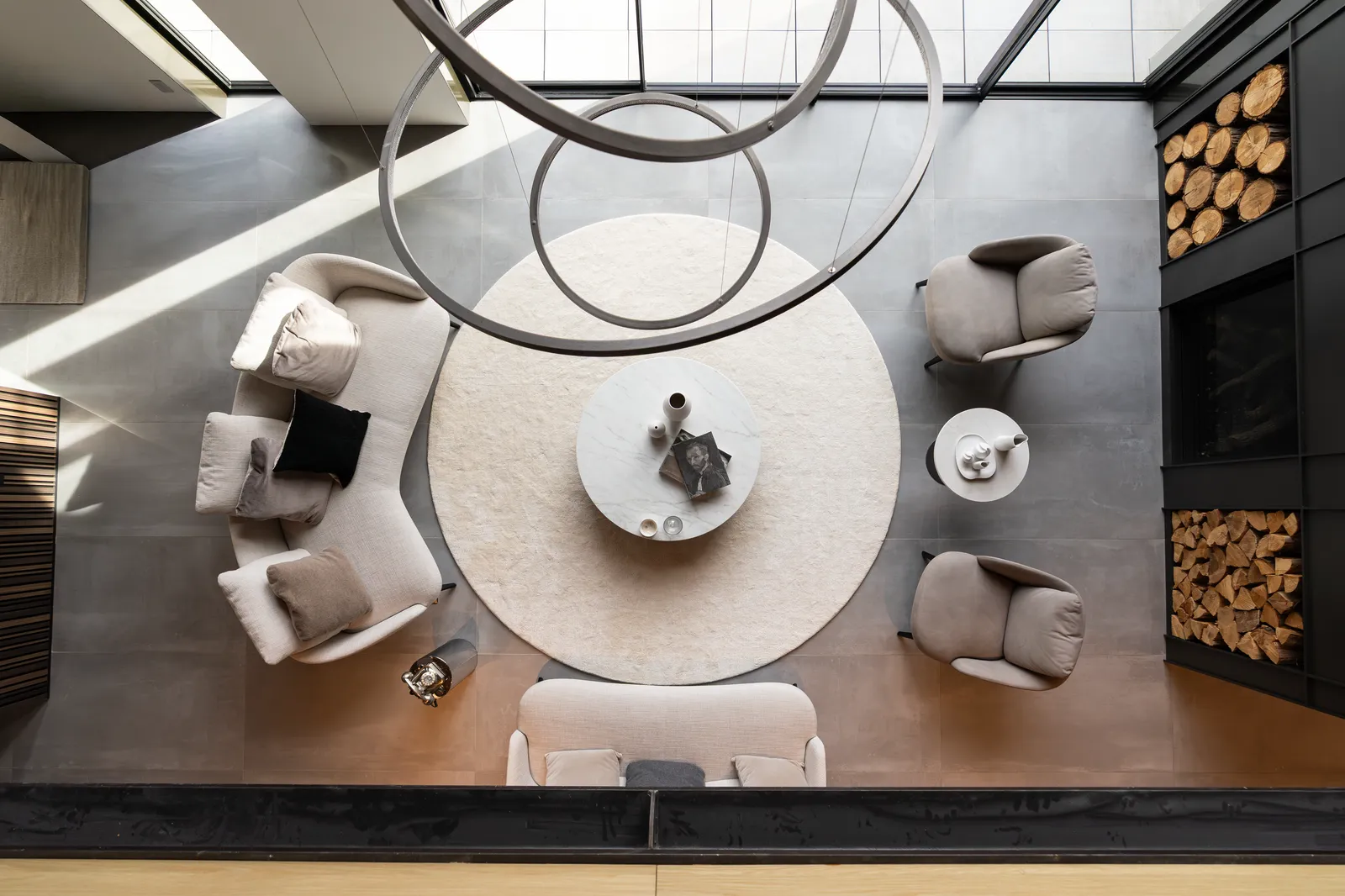 Overhead view of a round seating area under a sculptural ring chandelier, with stacked firewood