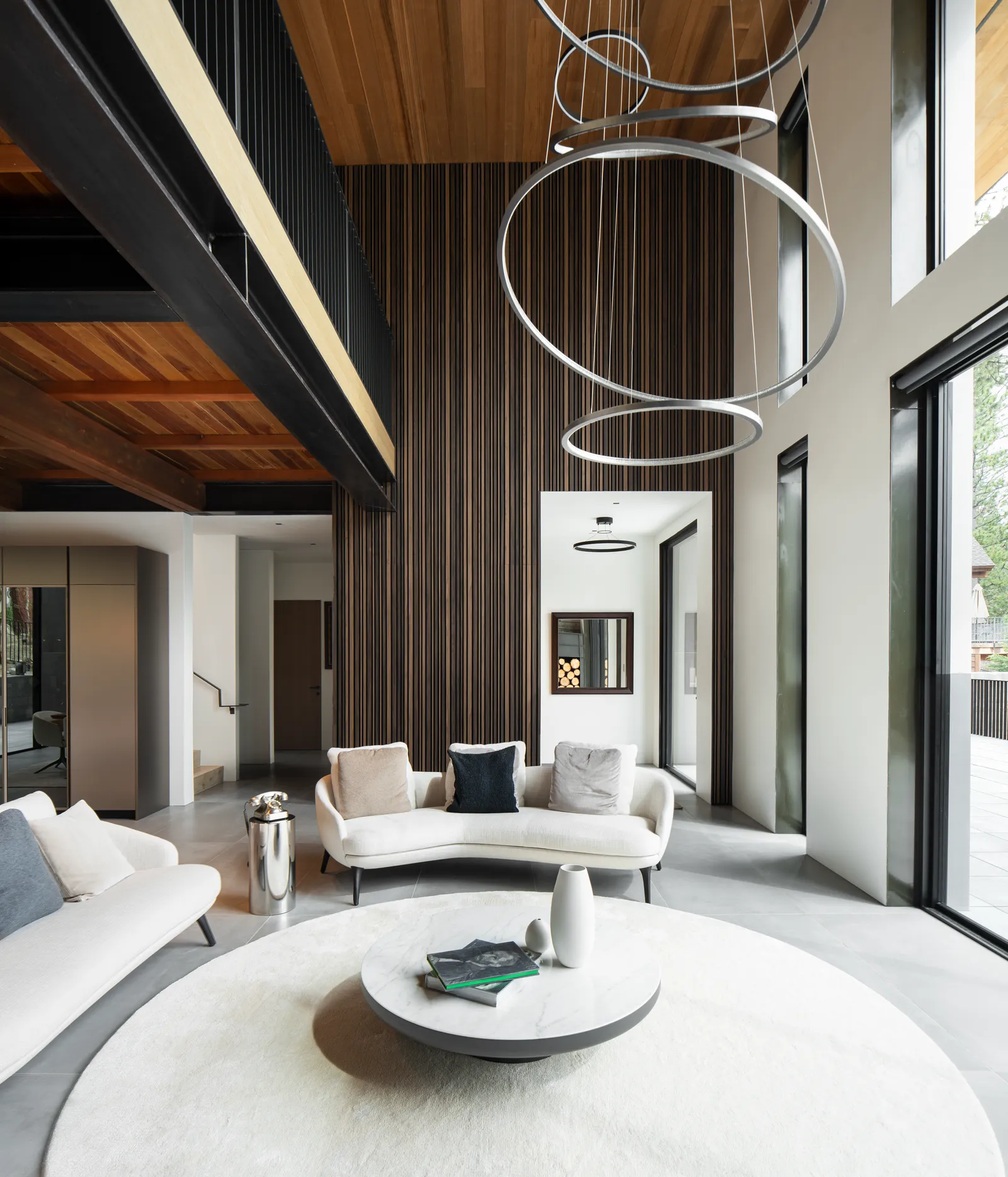 Double-height living room with a ring chandelier and a wood slat wall
