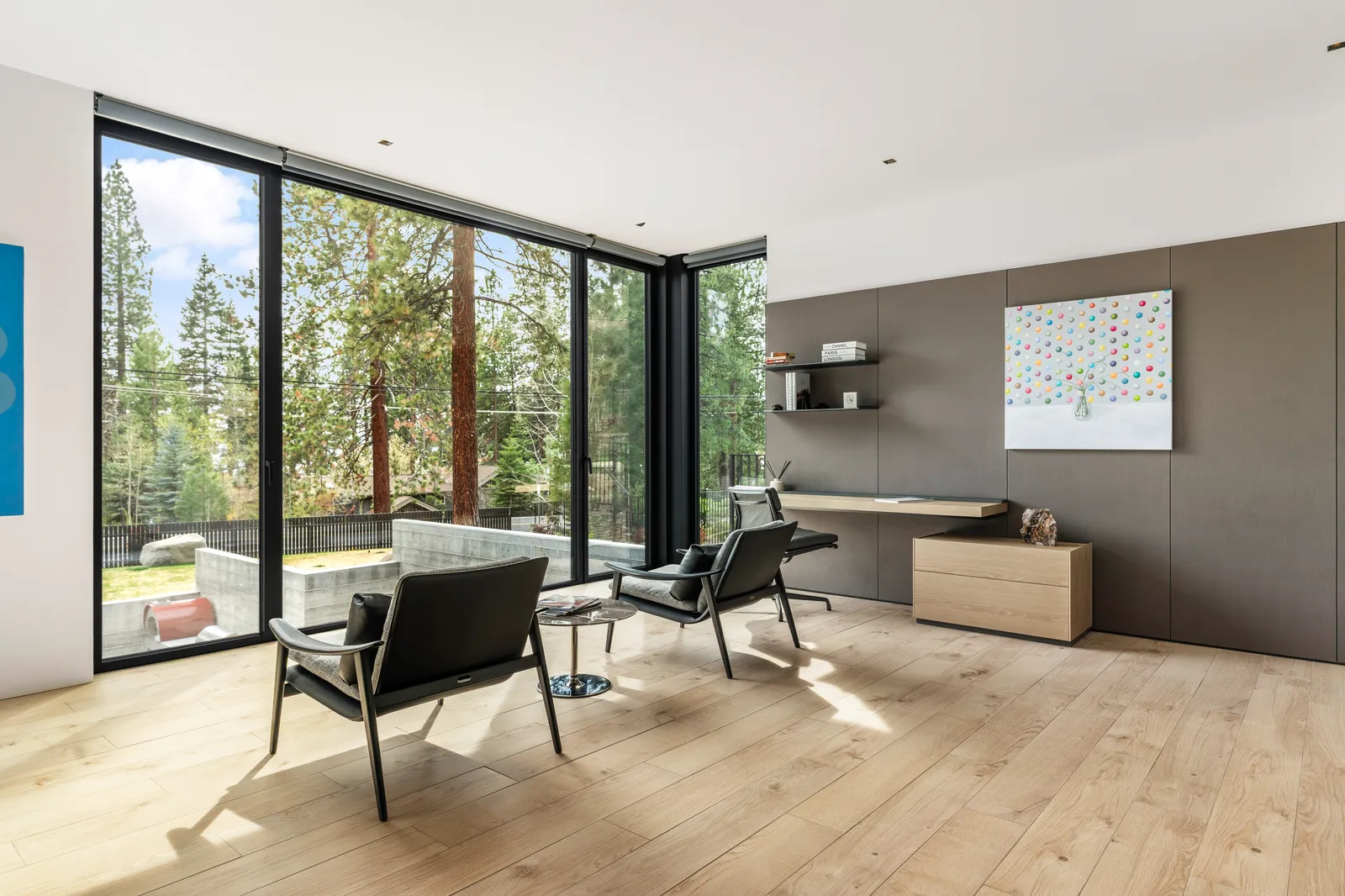 Sitting room with leather chairs and a desk facing tall windows to the forest